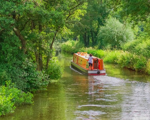 image of a person steering a narrowboat around a bend in the canal